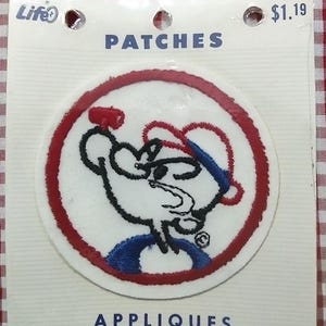 May include: A round patch featuring a cartoon character in a baseball cap, holding a red object. The patch is white with a red border and blue and black accents. The packaging reads "PATCHES" and "APPLIQUES".
