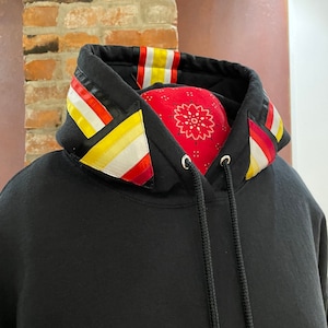 May include: Black hooded sweatshirt with a colorful striped trim around the hood. The trim features red, yellow, and white stripes.