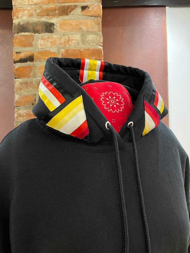 May include: Black hooded sweatshirt with a colorful striped trim around the hood. The trim features red, yellow, and white stripes.