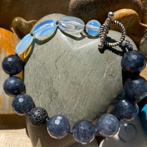 May include: A beaded bracelet with dark gray faceted beads, a black lava bead, and three oval-shaped white opal beads. The bracelet has a silver toggle clasp.