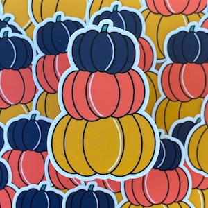 May include: A stack of three pumpkin stickers. The top pumpkin is dark blue, the middle pumpkin is orange, and the bottom pumpkin is yellow.