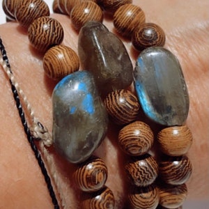 May include: A bracelet made of brown wooden beads and two dark gray stones. The bracelet is worn on a person's wrist.