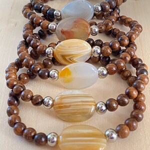 May include: Five wooden bracelets with agate stone beads. Each bracelet features a different colored agate stone with brown wood beads.