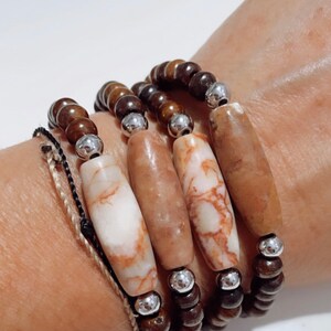 May include: A set of four bracelets with brown wooden beads and silver spacers. The bracelets feature four large, light brown, marbled, oval-shaped beads.