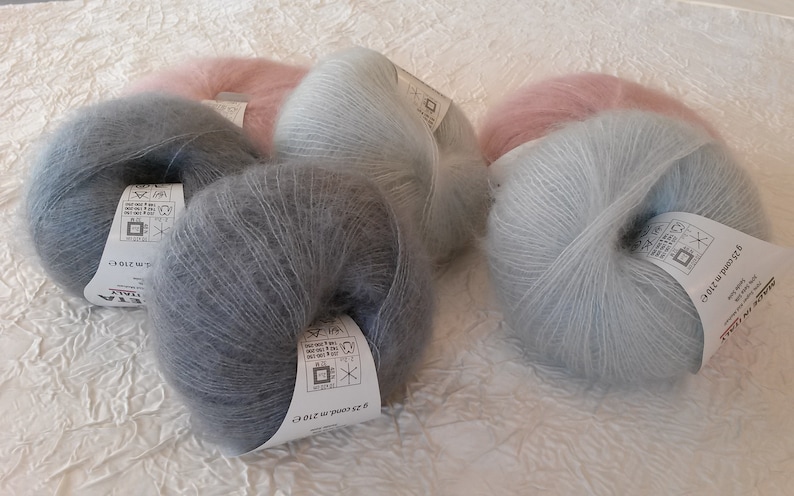 May include: Four skeins of yarn in different colors: gray, light blue, and pink. Each skein is wrapped in a circle and has a label with the brand name "Filati" and the yarn weight in grams.