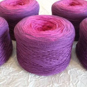 Può includere: Cinque gomitoli di lana in tonalità rosa e viola. La lana è sfumata, con un colore rosa più chiaro nella parte superiore e un colore viola più scuro nella parte inferiore.