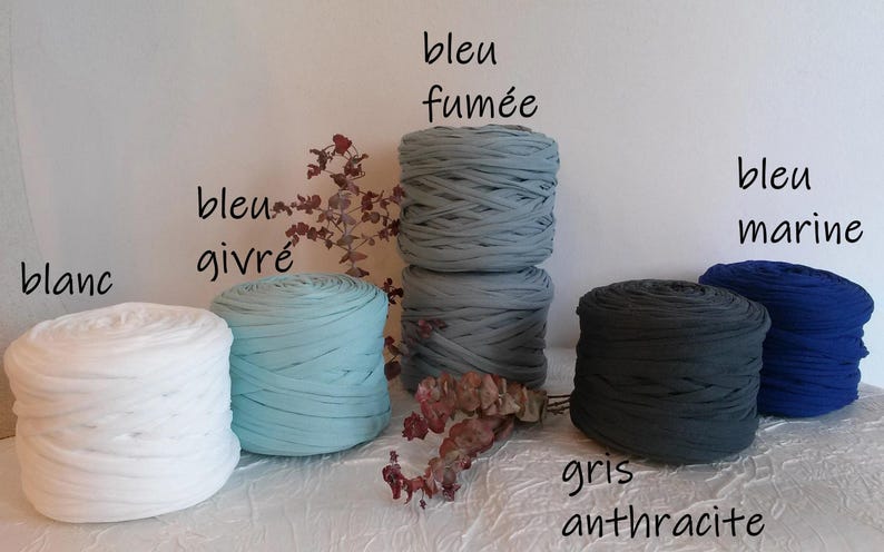 May include: A collection of colorful fabric yarn rolls in white, light blue, gray, dark gray, and blue. The image includes text labels in French: blanc, bleu givr&eacute;, bleu fum&eacute;e, gris anthracite, and bleu marine.