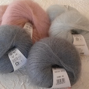 May include: Three skeins of yarn in different colors: light pink, light blue, and gray. The yarn is soft and fluffy, and the skeins are labeled with care instructions.