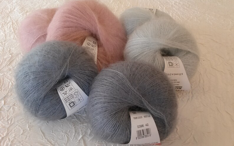 May include: Three skeins of yarn in different colors: light pink, light blue, and gray. The yarn is soft and fluffy, and the skeins are labeled with care instructions.