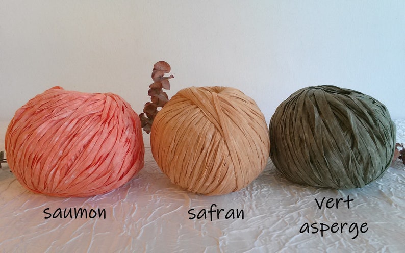 May include: Three balls of yarn in different colors: salmon, saffron, and green. The yarn is made of thin strips of fabric and is arranged in a ball shape.