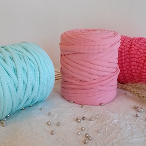 May include: Three spools of yarn in different colors: light blue, pink, and bright pink. The yarn is thick and textured, perfect for crocheting or knitting.