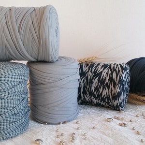 May include: An assortment of fabric rolls in various colors and patterns. There are several rolls of gray fabric, one with a checkered pattern, and another in a dark blue hue. A decorative pillow with a black and white pattern is also present.