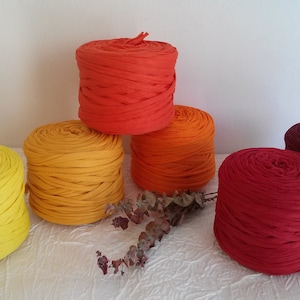 May include: Six spools of yarn in various shades of orange, red, and yellow. The yarn is arranged in a pyramid shape.