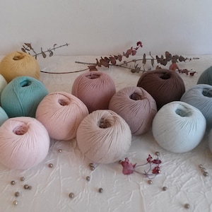 May include: A collection of yarn balls in various shades of pink, blue, brown, and beige. The yarn is arranged in a circle on a white surface.