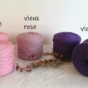 May include: Image of several spools of fabric yarn in shades of pink and purple. The colors are labeled "rose", "vieux rose", and "violet". The yarn is arranged on a white surface.