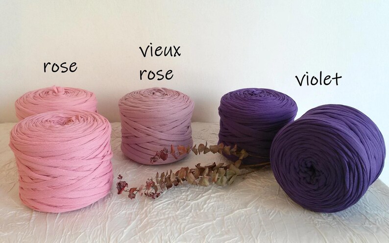 May include: Image of several spools of fabric yarn in shades of pink and purple. The colors are labeled "rose", "vieux rose", and "violet". The yarn is arranged on a white surface.
