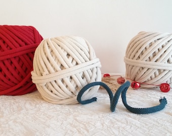 May include: Three balls of yarn, one red, one natural white, and one teal blue. The balls of yarn are on a white surface with red bells and a gold ribbon.