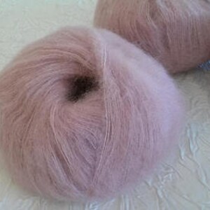 May include: A skein of soft, light pink mohair yarn. The yarn is fluffy and has a subtle sheen.
