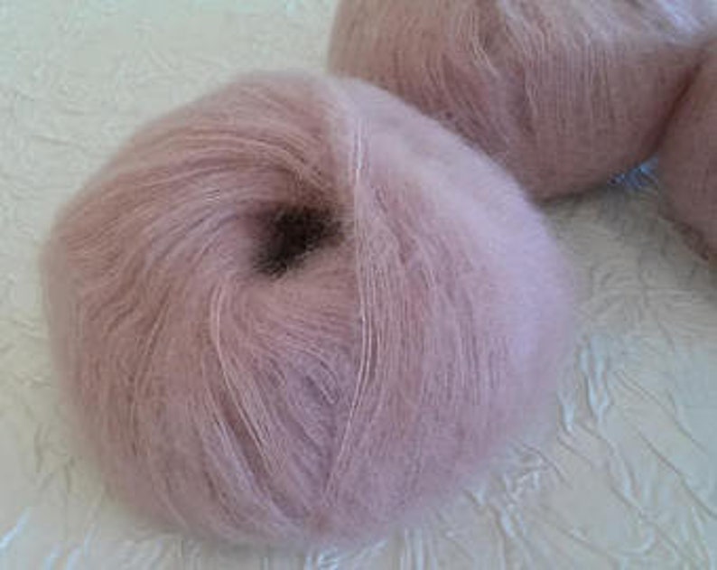 May include: A skein of soft, light pink mohair yarn. The yarn is fluffy and has a subtle sheen.