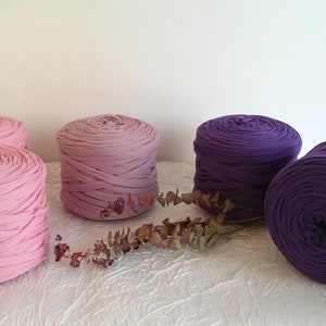May include: Four spools of yarn in pink, purple, and a gradient of pink to purple. The yarn is made of soft, stretchy fabric and is perfect for crafting.