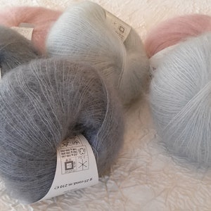 May include: Five skeins of soft, fuzzy yarn in shades of light blue, gray, and pink. Each skein has a white label with care instructions and the text "52 grams 210 m (230 yds)".