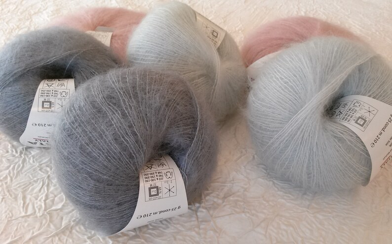 May include: Five skeins of soft, fuzzy yarn in shades of light blue, gray, and pink. Each skein has a white label with care instructions and the text "52 grams 210 m (230 yds)".