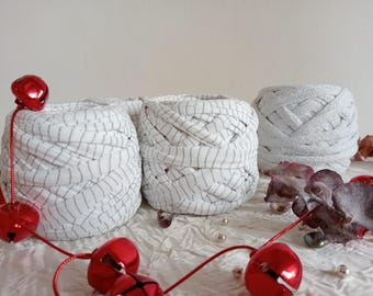 May include: Three white yarn balls with a woven pattern. The yarn is white with a thin black stripe. The yarn balls are on a white surface with red bells and a brown leaf.