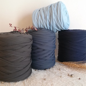 Op de afbeelding: Drie spoelen garen in verschillende kleuren: donkergrijs, donkerblauw en lichtblauw. Het garen is gemaakt van zacht, rekbaar materiaal en is perfect voor knutselen.