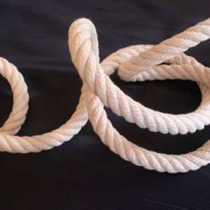 May include: A length of thick, off-white rope coiled into loops and curves. The rope has a tightly twisted construction, creating a textured surface. The background is a dark, solid color, providing contrast to the rope.