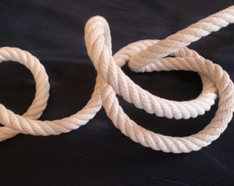 Könnte beinhalten: Ein Stück dickes, cremefarbenes Seil, das in Schlaufen und Kurven gewickelt ist. Das Seil hat eine eng gedrehte Konstruktion, wodurch eine strukturierte Oberfläche entsteht. Der Hintergrund ist eine dunkle, einfarbige Farbe, die einen Kontrast zum Seil bildet.