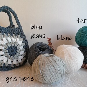 May include: A crocheted tote bag made with recycled t-shirt yarn in shades of gray, white, and turquoise. The yarn balls are labeled "bleu jeans", "blanc", "gris perle", and "turquoise".