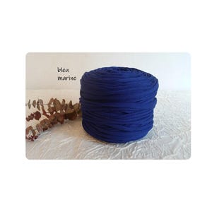 May include: A tightly wound roll of navy blue fabric, possibly jersey knit, sits on a white surface. The text "bleu marine" is visible in the upper left corner. Dried foliage adds a natural accent.