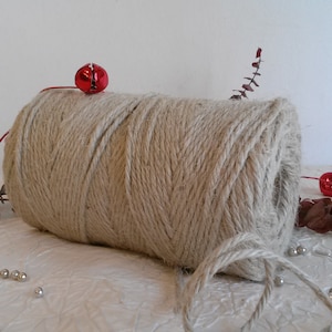 Può includere: Un rotolo di spago naturale di colore beige, avvolto in carta bianca. Lo spago è decorato con campanelle rosse e rametti di eucalipto essiccato.