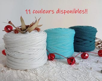 May include: Three spools of fabric in white, turquoise, and teal, arranged on a textured white surface. The white spool is decorated with dried leaves and red bells. The text "11 couleurs disponibles!!" is written in red.