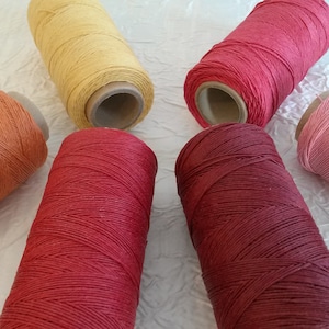 May include: Six spools of waxed cotton thread in various shades of red, orange, and yellow. The spools are arranged in a circle on a white surface.
