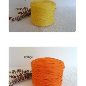 May include: Two spools of fabric yarn, one yellow and one orange, are displayed. The yellow spool is labeled "jaune" and the orange spool is labeled "orange". The yarn is tightly wound, and the spools are cylindrical.