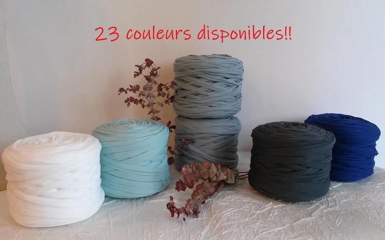May include: A collection of colorful fabric yarn rolls in white, light blue, gray, dark gray, and blue. The image includes the text "23 couleurs disponibles!!" in red, indicating a variety of color options.