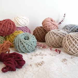 May include: A collection of colorful cotton rope yarn in various shades of green, red, brown, beige, white, and blue. The yarn is arranged in a pile on a white surface with decorative beads scattered around.