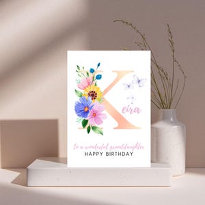 May include: A white birthday card with a floral design and the letter "K". The card features a watercolor illustration of colorful flowers, butterflies, and the name "Eira". The text reads "To a wonderful granddaughter, Happy Birthday."
