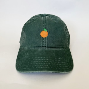 Może przedstawiać: Ciemnozielona czapka z daszkiem z haftowaną pomarańczą z zielonym listkiem z przodu.