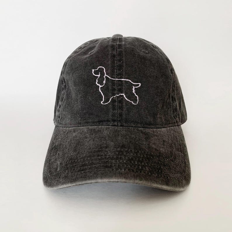 May include: A black baseball cap with a white embroidered outline of a cocker spaniel.