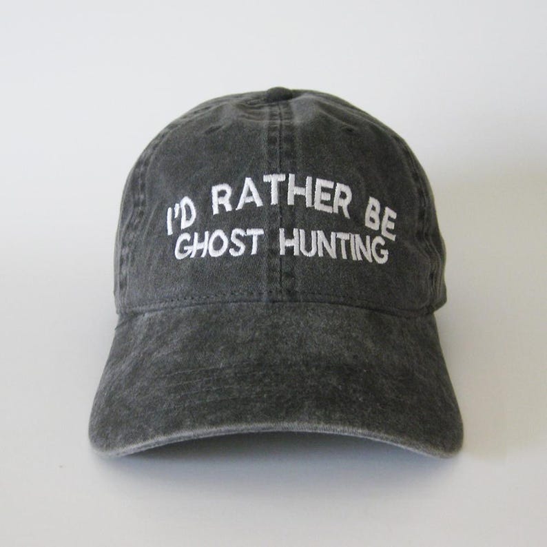 Może przedstawiać: Czarna czapka z daszkiem z haftem "I'd rather be ghost hunting" w kolorze białym.