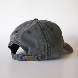May include: A charcoal gray baseball cap with a curved brim. The cap features a metal clasp for adjustment and a small button on top. The fabric appears to be pre-washed for a vintage look.