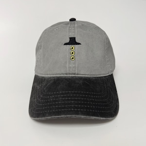 Puede incluir: Gorra de béisbol gris con visera negra. La gorra presenta un diseño bordado de un sombrero negro y tres círculos amarillos. El sombrero está hecho de una tela suave y duradera y tiene una correa ajustable.