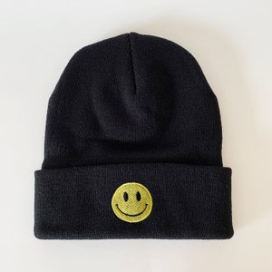 Puede incluir: Gorro negro con una cara sonriente amarilla bordada en la parte delantera.