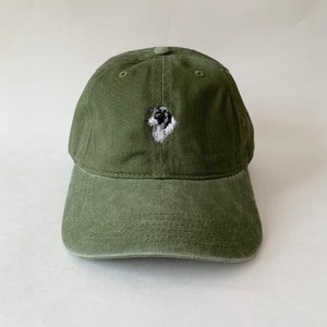 Könnte beinhalten: Eine grüne Baseballkappe mit einem gestickten Bild eines schwarz-weißen Hundes auf der Vorderseite.