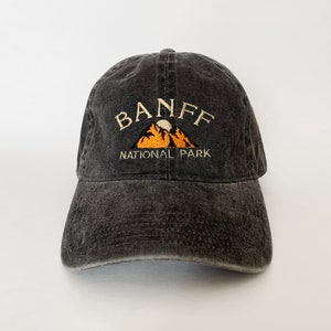 May include: A black, distressed, cotton baseball cap with an embroidered design of a mountain range with a moon and the text "BANFF NATIONAL PARK".