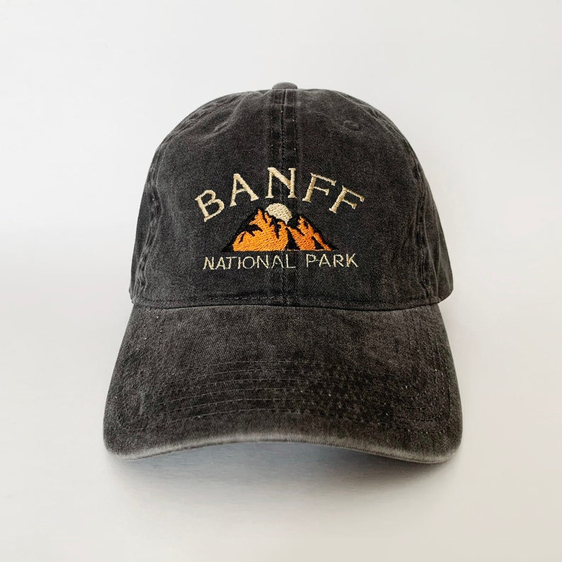 May include: A black, distressed, cotton baseball cap with an embroidered design of a mountain range with a moon and the text "BANFF NATIONAL PARK".