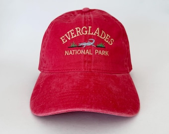 May include: Red baseball cap with an embroidered Everglades National Park logo featuring an alligator. The logo is in white and gold lettering.