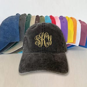 May include: A black washed cotton baseball cap with a gold embroidered monogram "SKY" on the front. The cap is displayed with a variety of other colored baseball caps in the background.